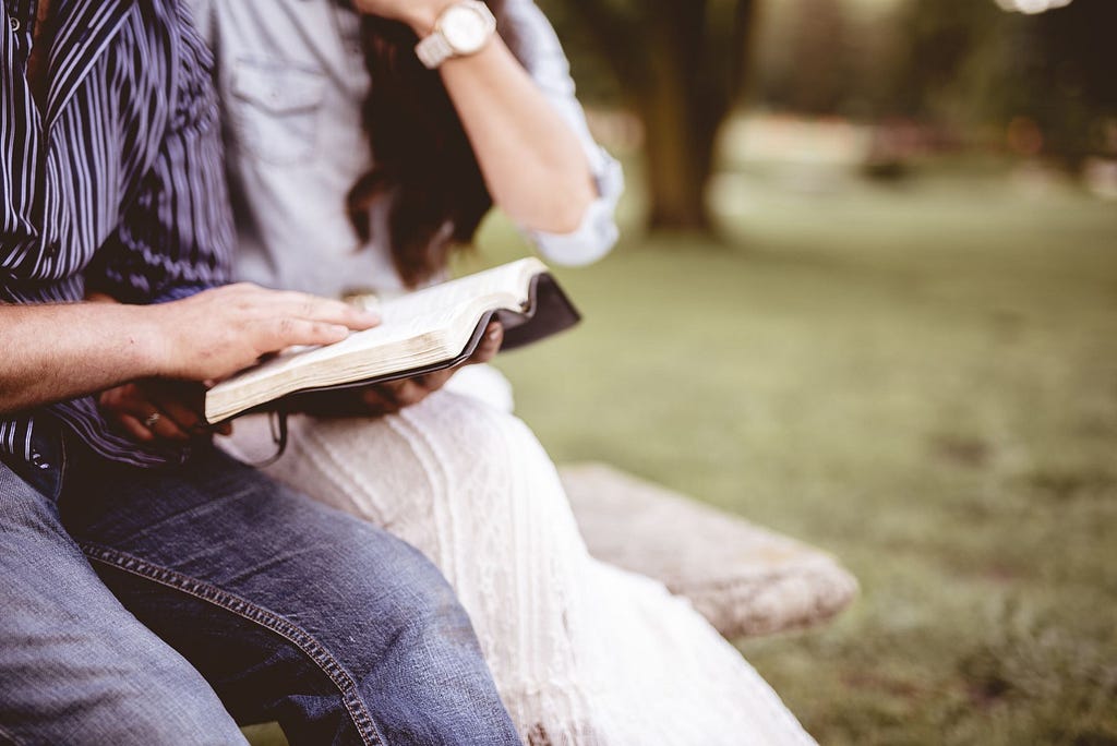 A photo of a man reading the Bible to someone