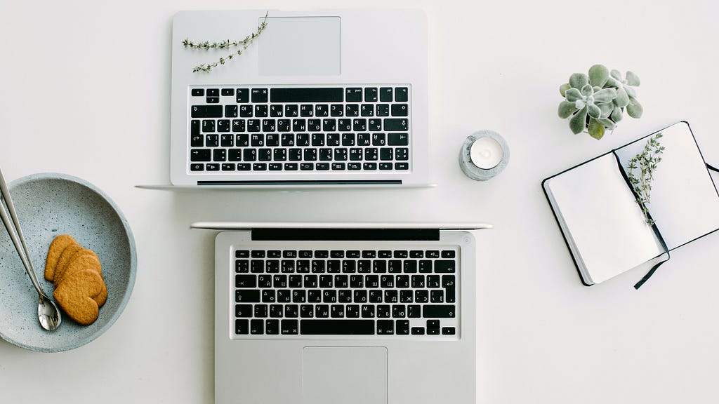 Two Macbooks standing back to back, next to a bowl with cookies and a notebook.