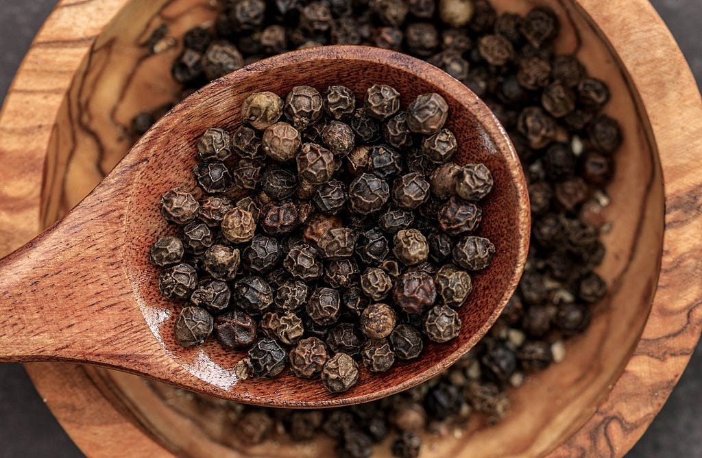 black peppercorns scooped from a full bowl into a wooden spoon