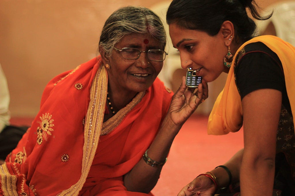 An aged woman using a mobile phone assisted by a frontline worker