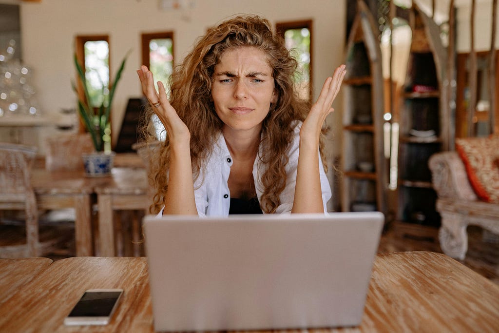 Photo of an frustrated woman sitting by the laptop.