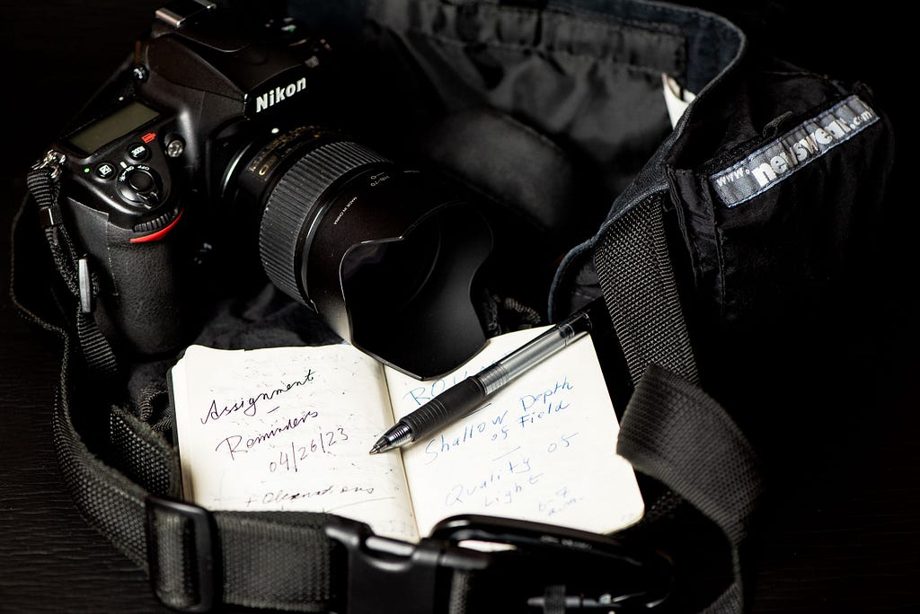 A display of a camera bag, camera with lens attached, and a pocket notebook with pen for note taking duties. Oberhausen, Germany, April 26, 2023.