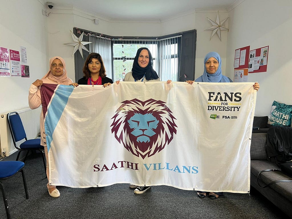 4 women proudly holding a saffron Saathi Villans flag in the Saathi House office.