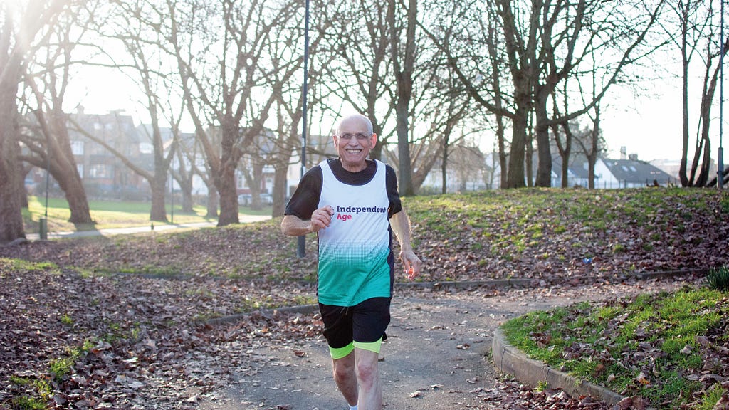 Older man running in park wearing training vest with Independent Age logo