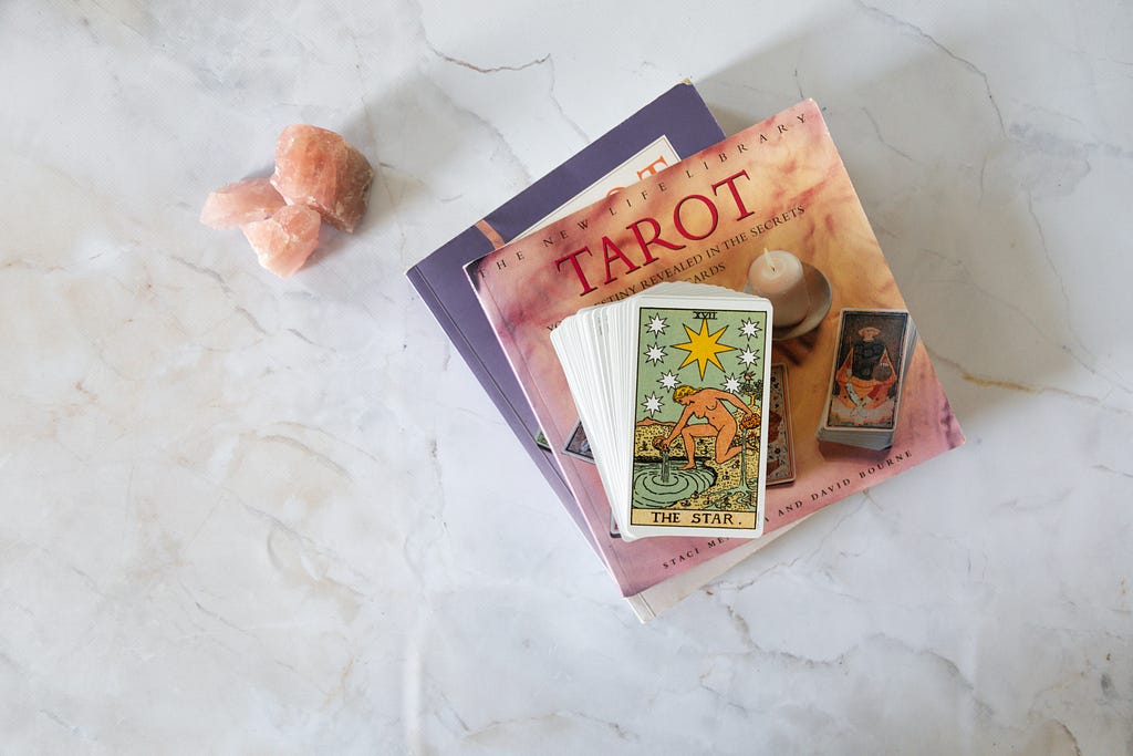 A deck of tarot cards sits atop a neat stack of tarot books against a backdrop of crisp white marble.