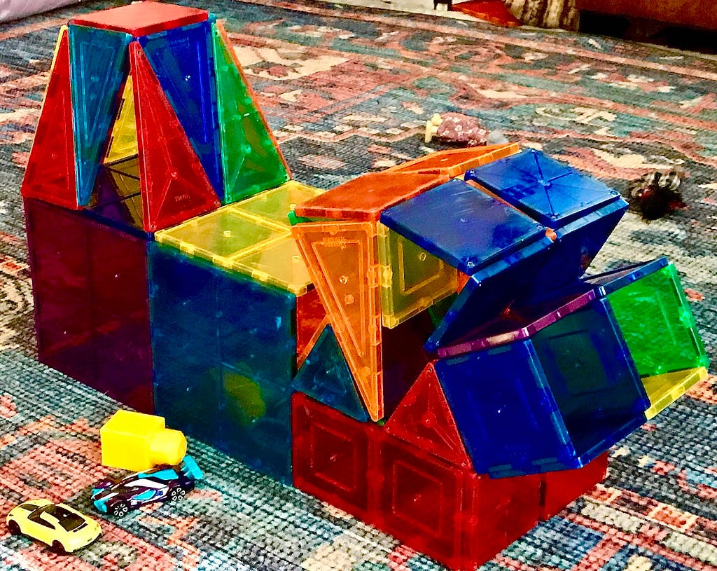 multi-color magna-tiles, children’s construction toys, in shape of a futuristic building, with other toys