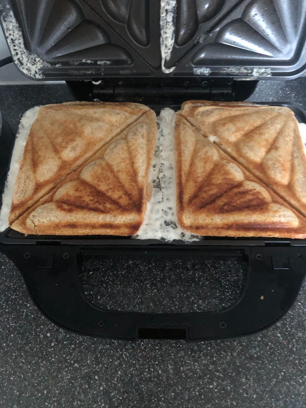 A toastie sandwich machine with two sandwiches leaking the filling all over the machine, leaving a mess.