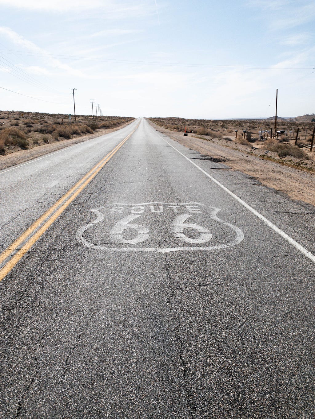 empty 2 lane road in the desert. Big ‘Route 66’ logo printed on the right lane of the road