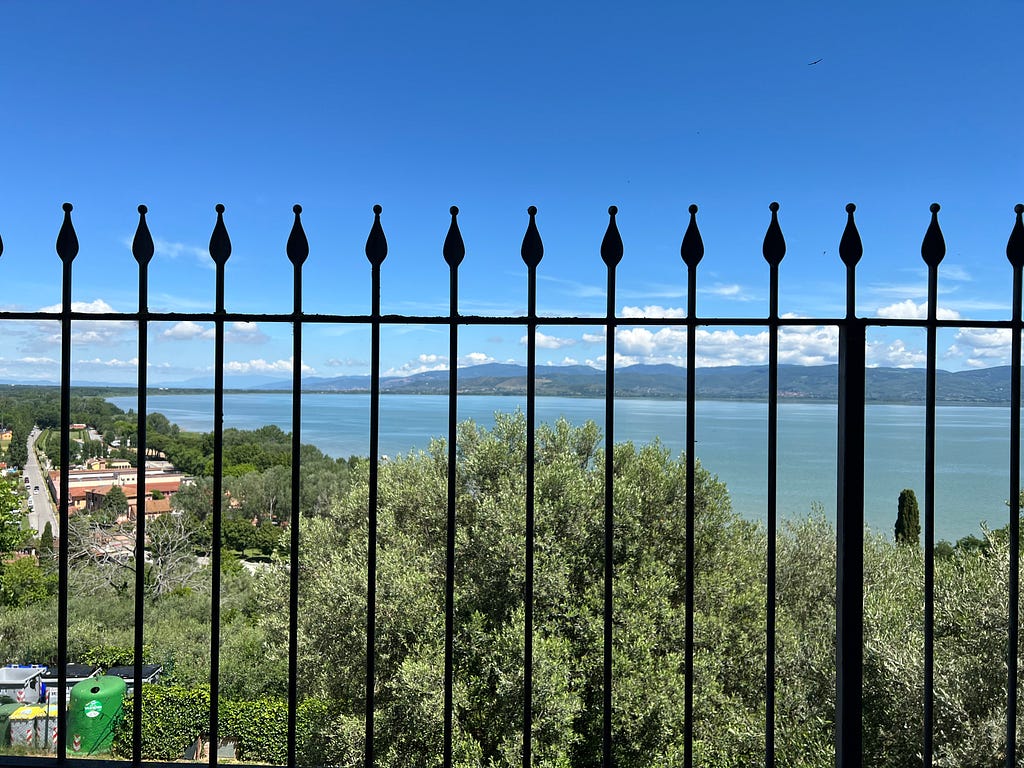 Photo of an Italian lake from the atop the cliffs of the adjacent city. A fence obstructs the view.