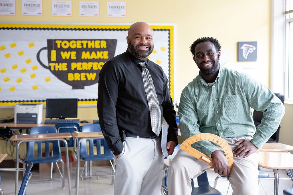 Two male teachers of color smile at the camera.