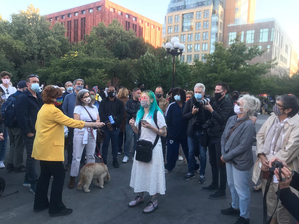 Event organizer Ke Walcott addressing the gathered crowd with a reporter holding a microphone in front of her.