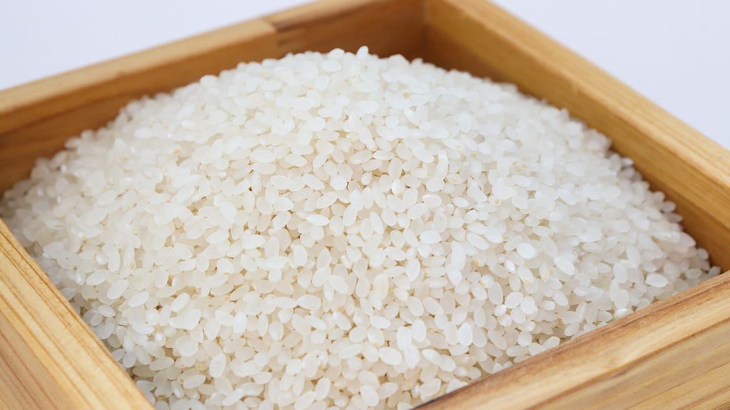 Zdjęcie małej, drewnianej skrzynki pełnej ziaren białego ryżu