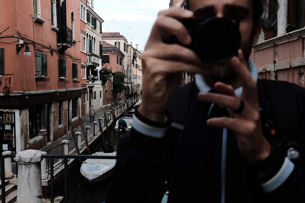 blurry man with camera pointing in foreground; sharpened Venice canal in the background