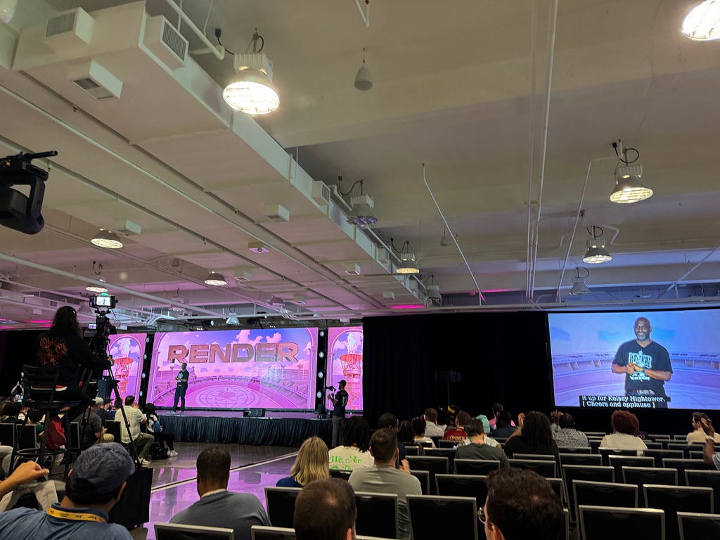 Kelsey Hightower giving a keynote speech on the main stage while projected on large video monitors.