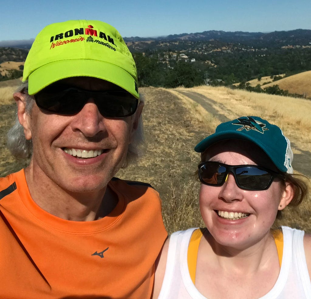A father and daughter enjoying a sunny trail run in hats and sunglasses