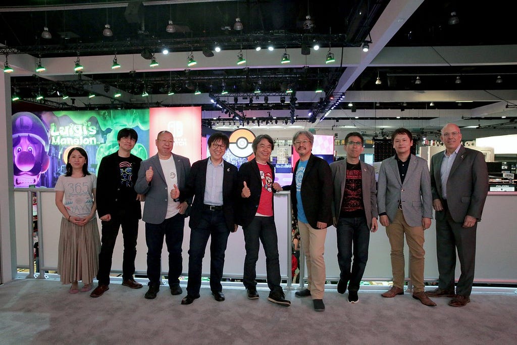 A group of Nintendo employees, executives, and legendary game developers gather for a photo above their June 2019 E3 showroom in the Los Angeles Convention Center.
