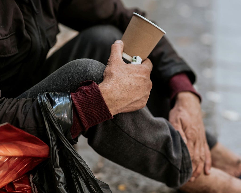 A photo of a homeless man holding a cup