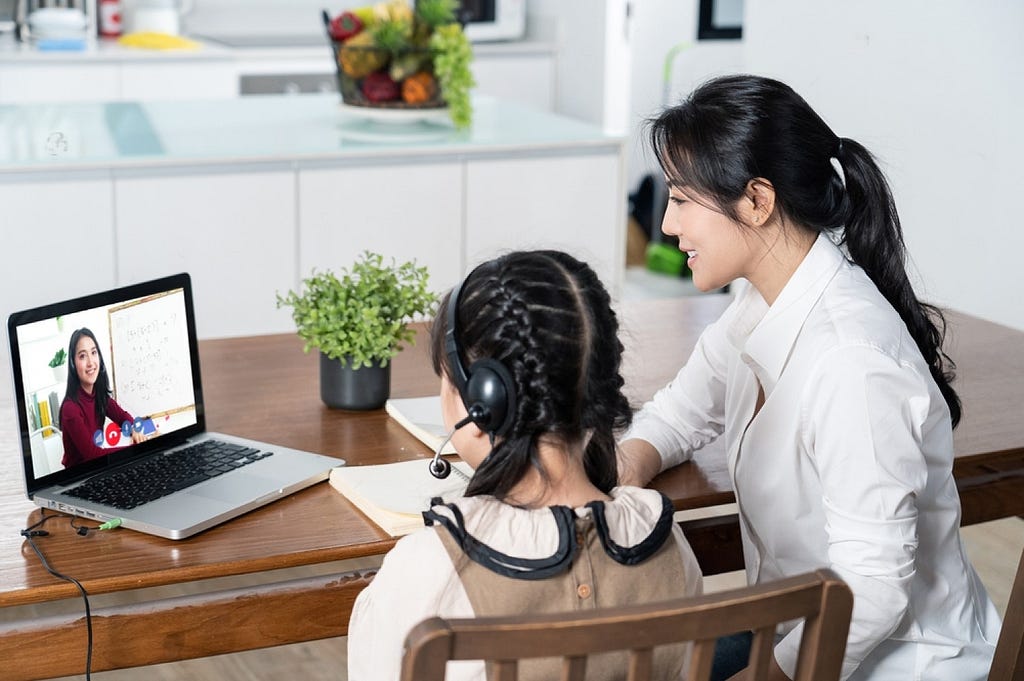 A woman and child engage in online learning, seated at a table with a laptop.