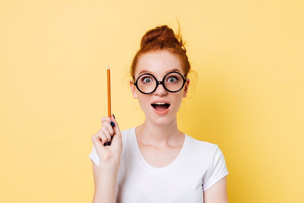 Woman holding pencil up with surprised look on her face. Yellow background.