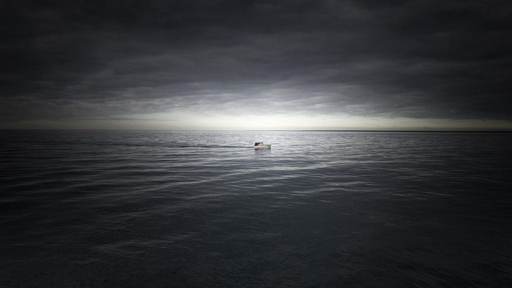 A single, tiny boat wanders in water, with a gray, overcast sky above.