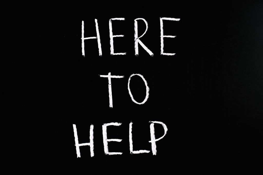 “Here to Help” is written in chalk on a black background.