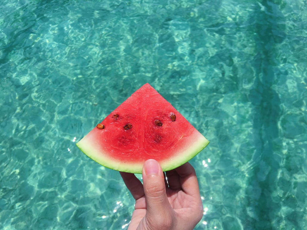 Hand holding a watermelon over pool water