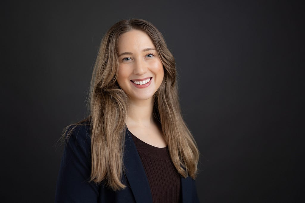Image of new Research Manager, Dr. Sarah Okey, on a black background wearing a dark shirt and navy blue blazer