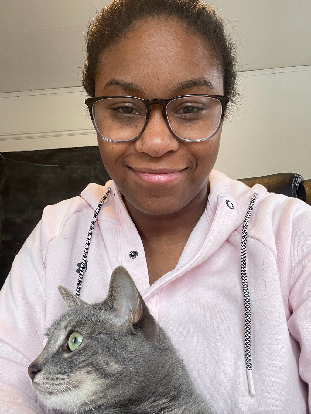 Natalie Cantave looking at the camera wearing glasses and holding her grey cat Pancake