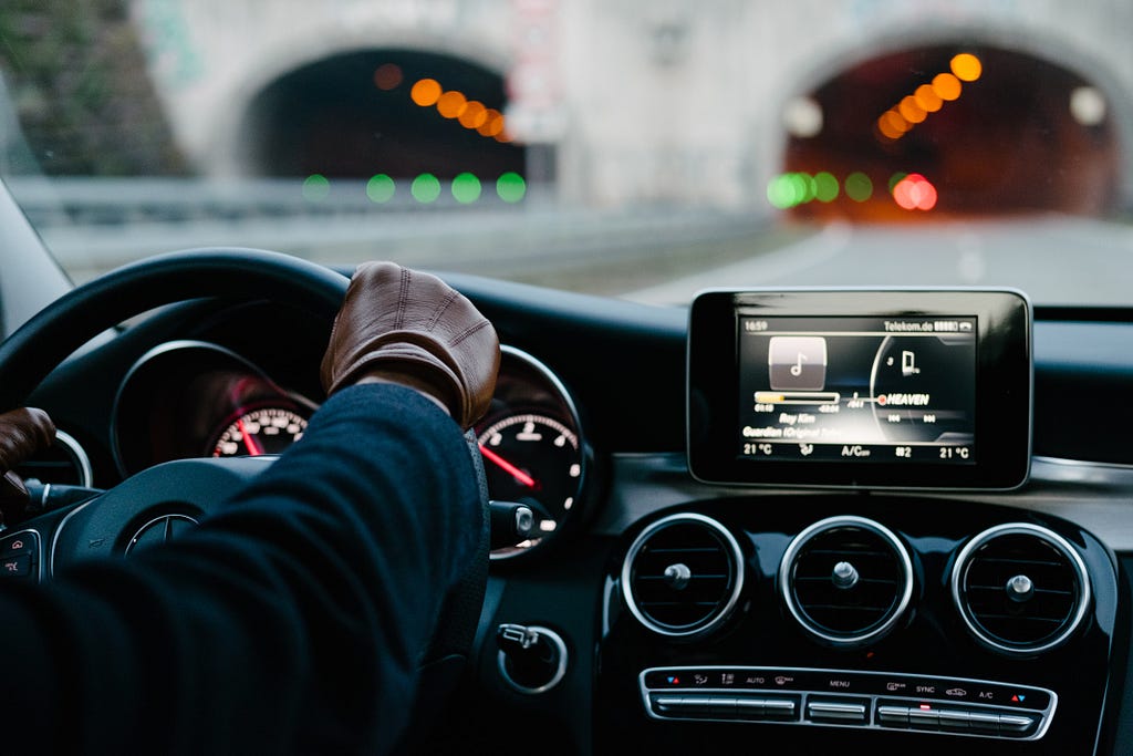 A person wearing brown leather gloves drives a car into a tunnel.