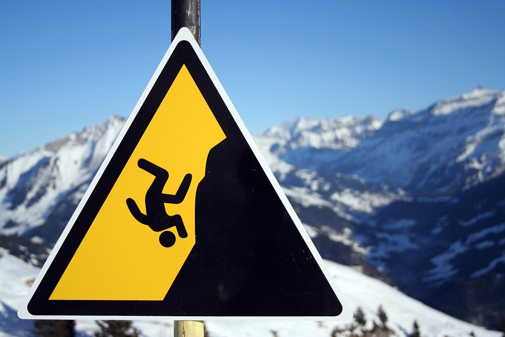 Fall hazard sign in front of snowy mountain landscape.