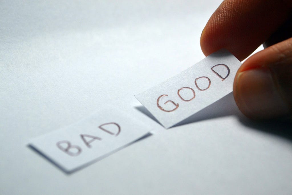 A photograph of a hand deciding whether to pick up a label that says “good” or a label that says “bad.”