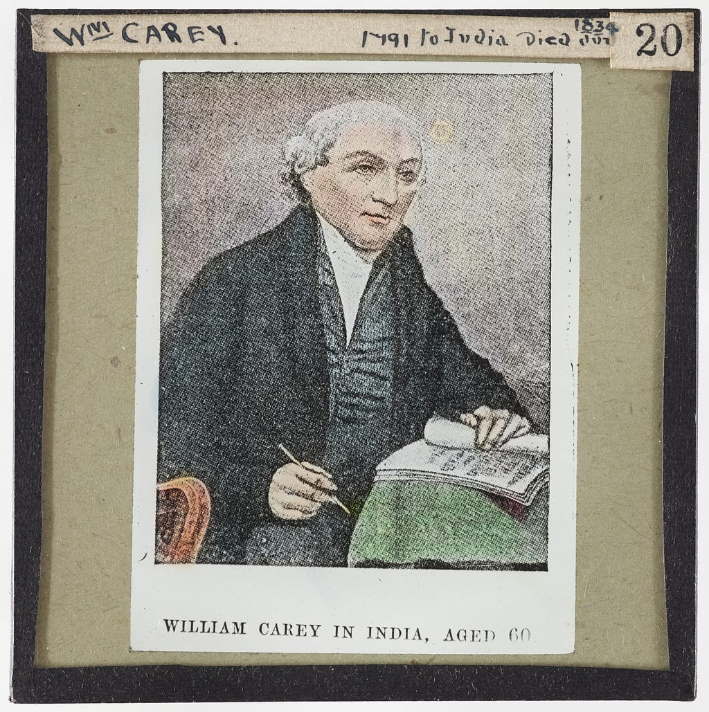 A painting of Carey seated writing in a book, accompanied with the text: “William Carey in India, aged 60”.