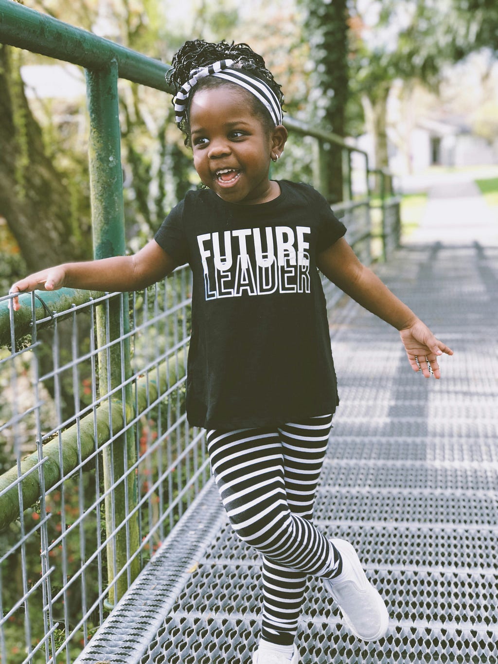 A young girl wearing black and white striped tights and a t-shirt that says “Future leader”.