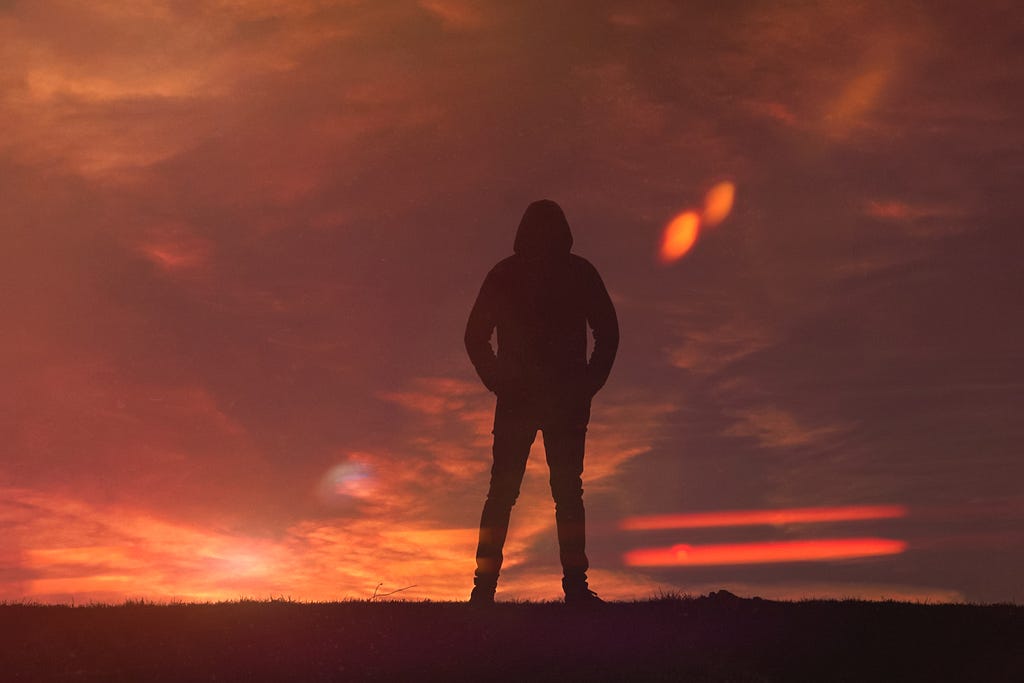 The silhouette of a man in a hoodie standing in front of a sunset.
