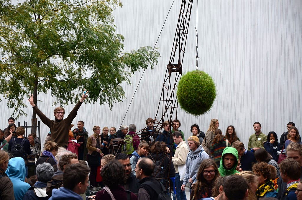 A ball of grass being raised by a crane — a scene at the 2014 Degrowth Conference, according to Wikipedia