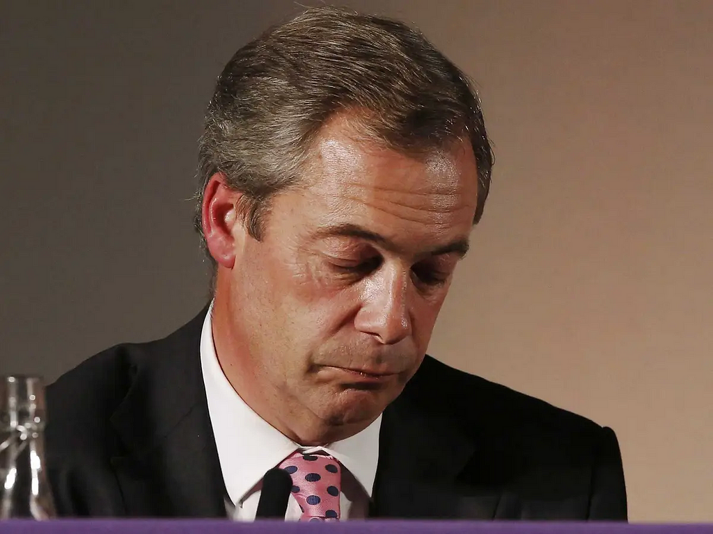 UK professional populist eejit Nigel Farage looking down with eyes closed, perhaps seeing a txt showing he is on course to once again not be elected as an MP.