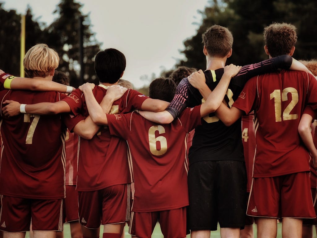 Imagem de meninos de um time de futebol abraçados de costas