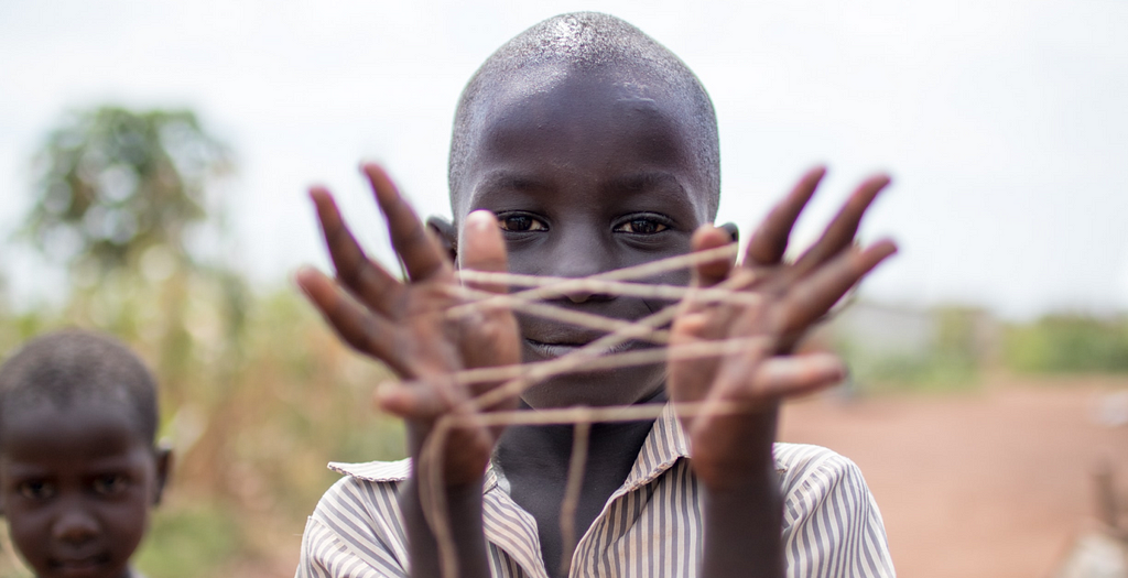 A picture of a black kid holding a shape made from thread between his fingers