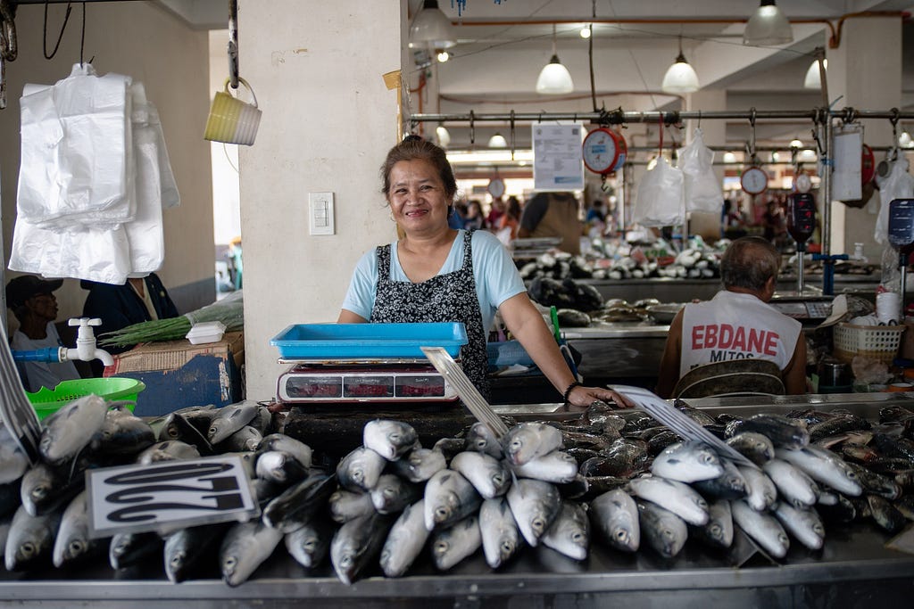 A woman behind her supply of fish for sale in a seafood market in the Philippines.