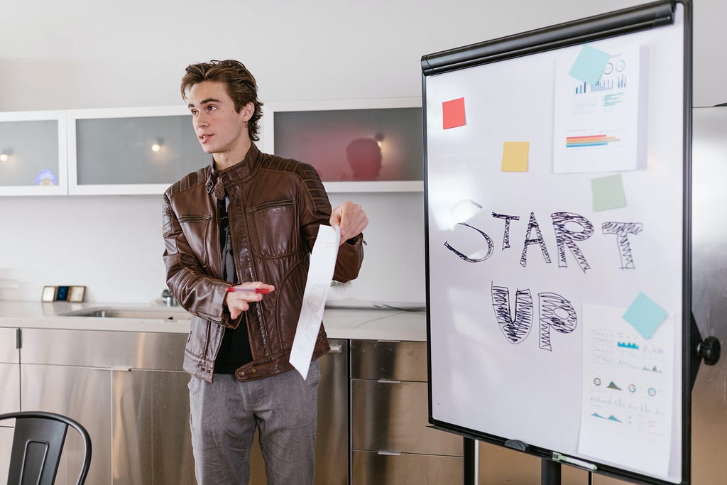 Young man giving a pitch with a blackboard that reads “startup”