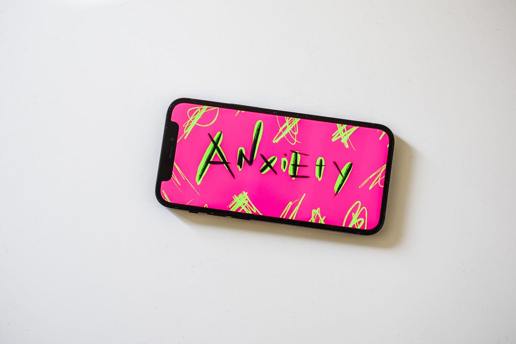 A mobile phone with Pink and background and Anxiety written in black and florescent green strokes.