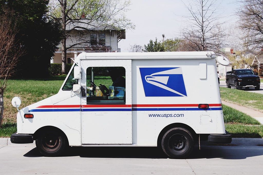 A US Postal Service truck parked on the curb in a residential neighborhood.