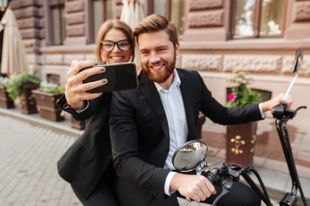 A man and woman in business attire smiling and taking a selfie together.