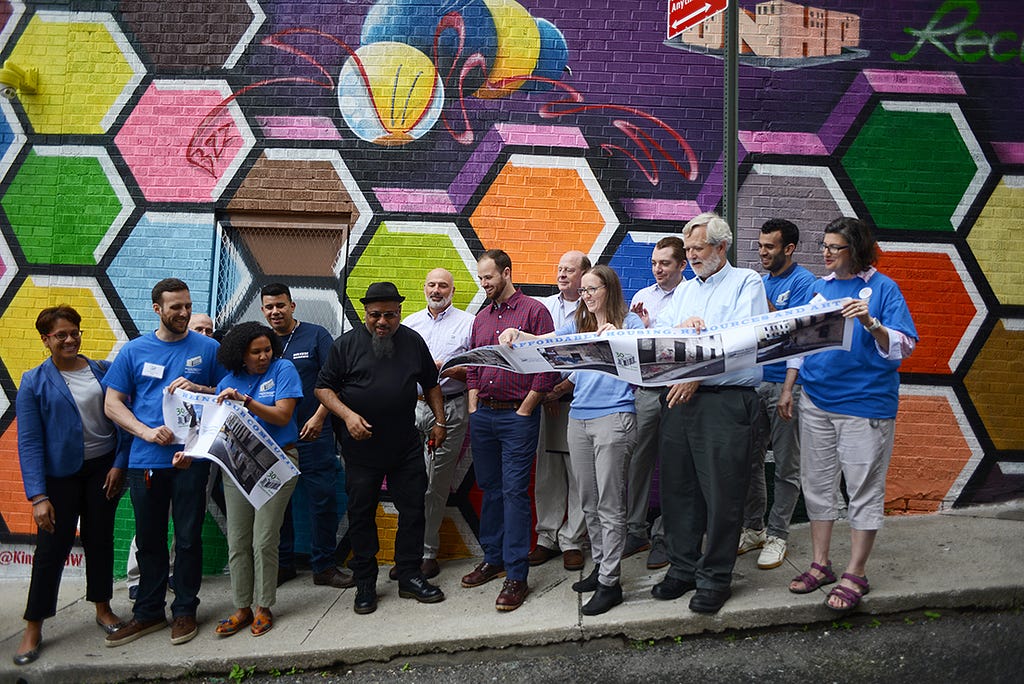A diverse group of people at a ribbon-cutting for a colorful mural