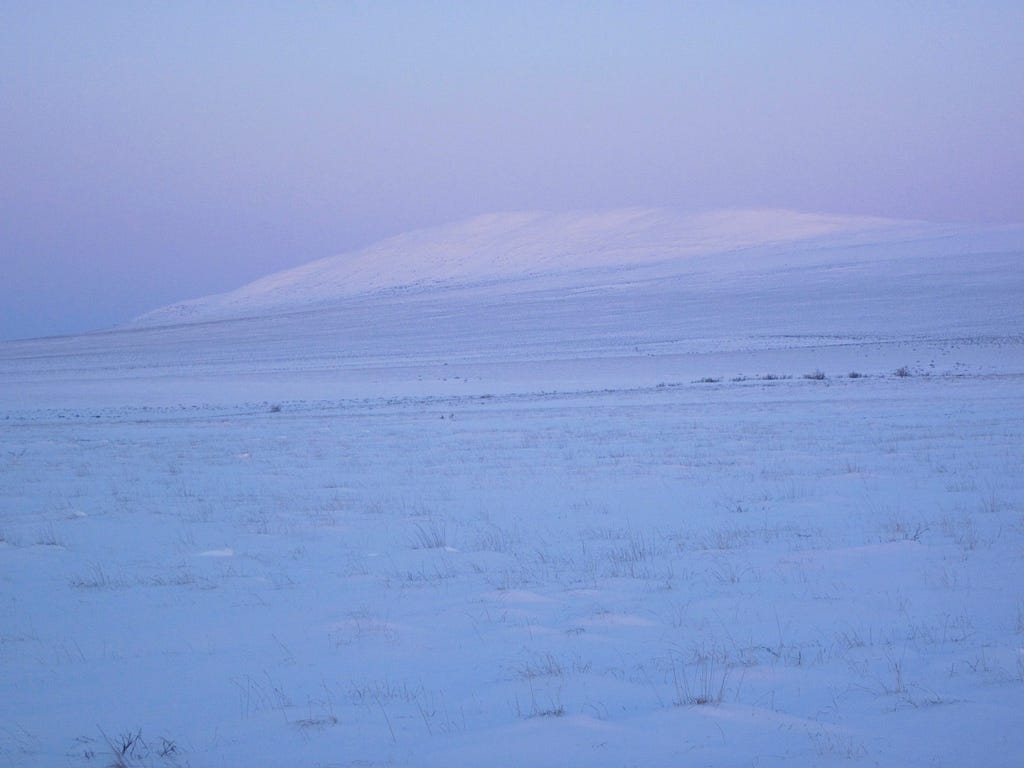 a pastel hued snow covered field with hill in the background