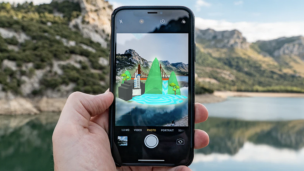 A hand holds up an iphone. The screen shows a mountain lake with 3D augmented reality elements superimposed on it.