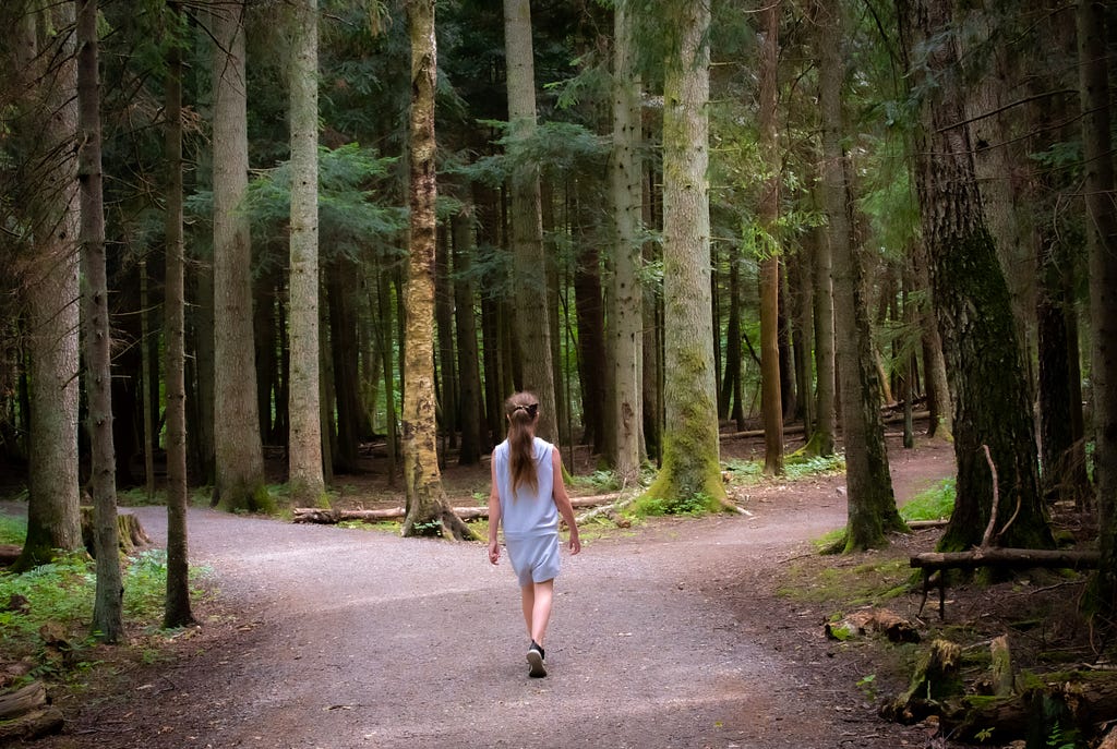 A girl standing before two diverging paths in the woods