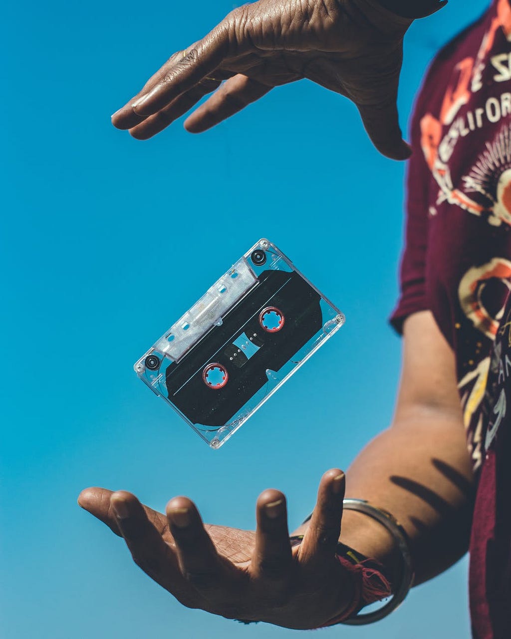 A record cassette floating in the air between two hands of a person