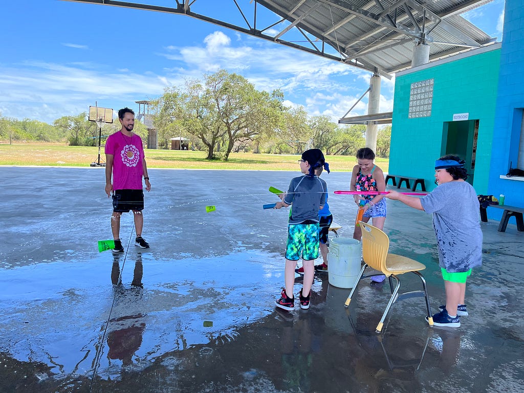 four campers use their waterguns to shoot water at fellow campers and our activity leader, word.