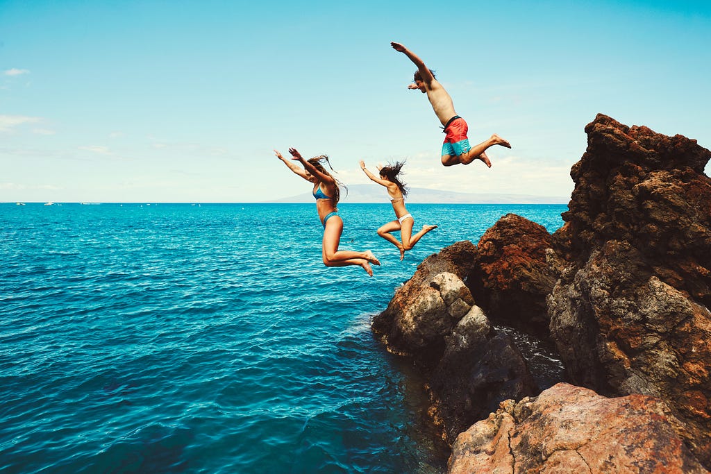 Three people leap off cliff into the ocean